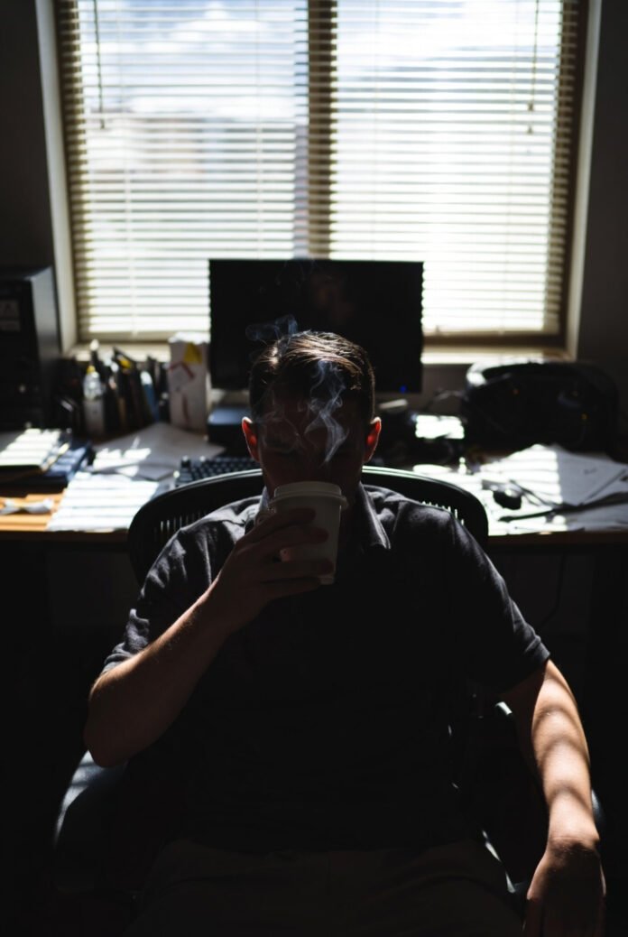 Tired worker slumps in chair with rising coffee steam and messy desk.