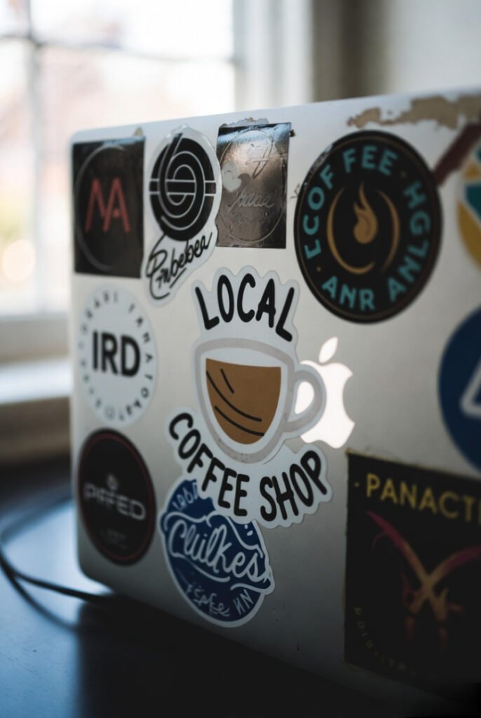 Old MacBook lid plastered with faded stickers, featuring a prominent local coffee shop logo.