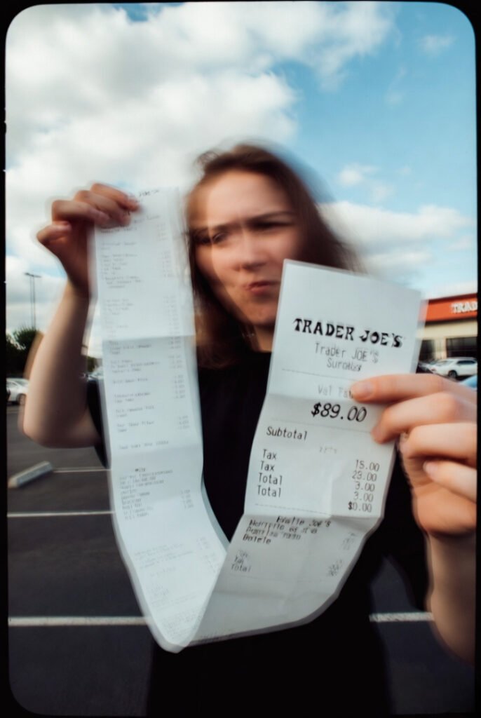 Blurry selfie in Trader Joe’s parking lot: person sighing while holding up a very long receipt totaling $89 for “just a few things.”