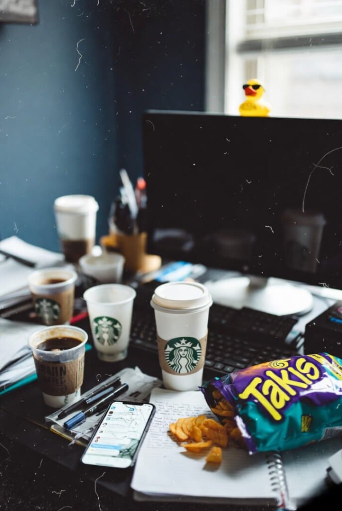 Blurred film-style home office scene: Starbucks mugs everywhere, notebook with urgent lead scribbles, Takis crumbs, cracked phone notifications, duck in shades watching